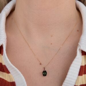 Gold necklace with a small oval green pendant resting on the base of the neck.