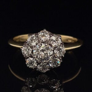 Gold ring with a cluster of diamonds arranged in a flower shape on a black background, close-up.