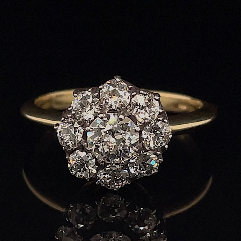 Gold ring with a cluster of diamonds arranged in a flower shape on a black background, close-up.