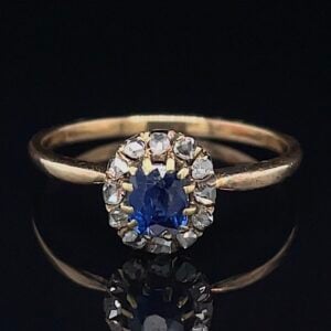 Gold ring with an oval blue sapphire haloed by small diamonds on a yellow-gold band, set against a dark background.
