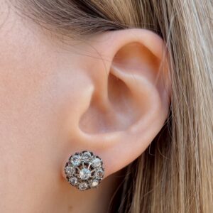Close-up of an ear wearing a round, floral diamond cluster stud earring in a silver setting.
