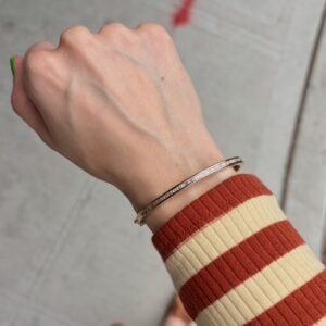 Close-up of a wrist with a slim rose-gold bracelet worn over a red-and-cream striped sweater cuff.