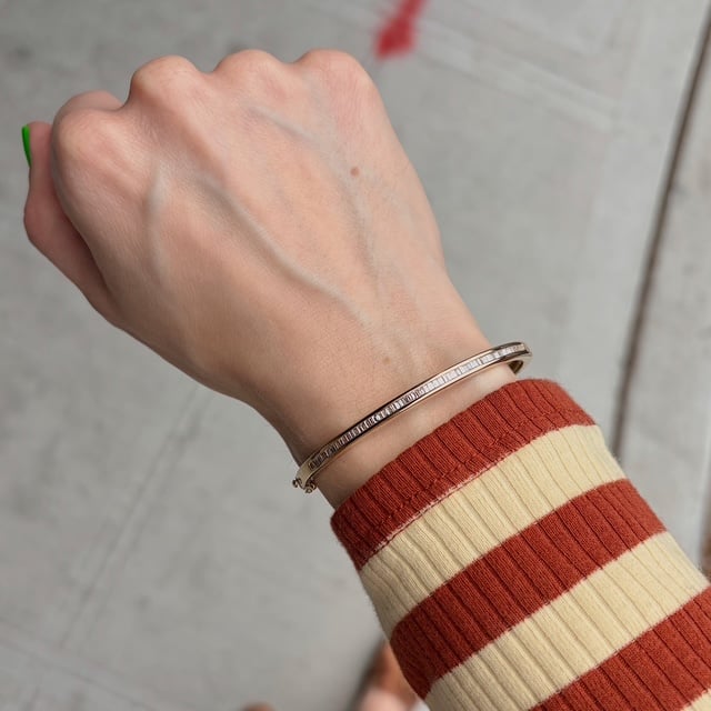 Close-up of a wrist with a slim rose-gold bracelet worn over a red-and-cream striped sweater cuff.