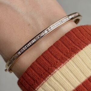 Rose gold bangle with a row of sparkling baguette diamonds on the wrist, cuffed by a striped red and beige sweater sleeve.