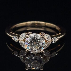 Engagement ring with a large round center diamond and small side stones in a gold setting on a black background, shown from above.