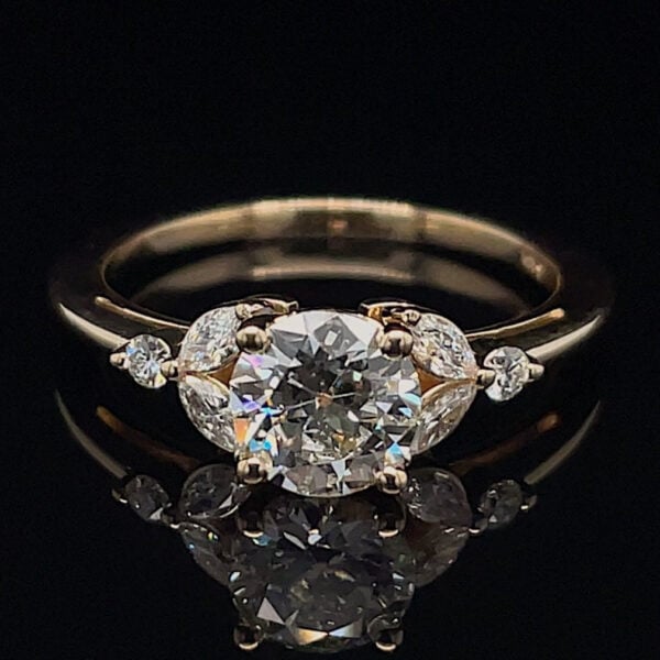 Engagement ring with a large round center diamond and small side stones in a gold setting on a black background, shown from above.