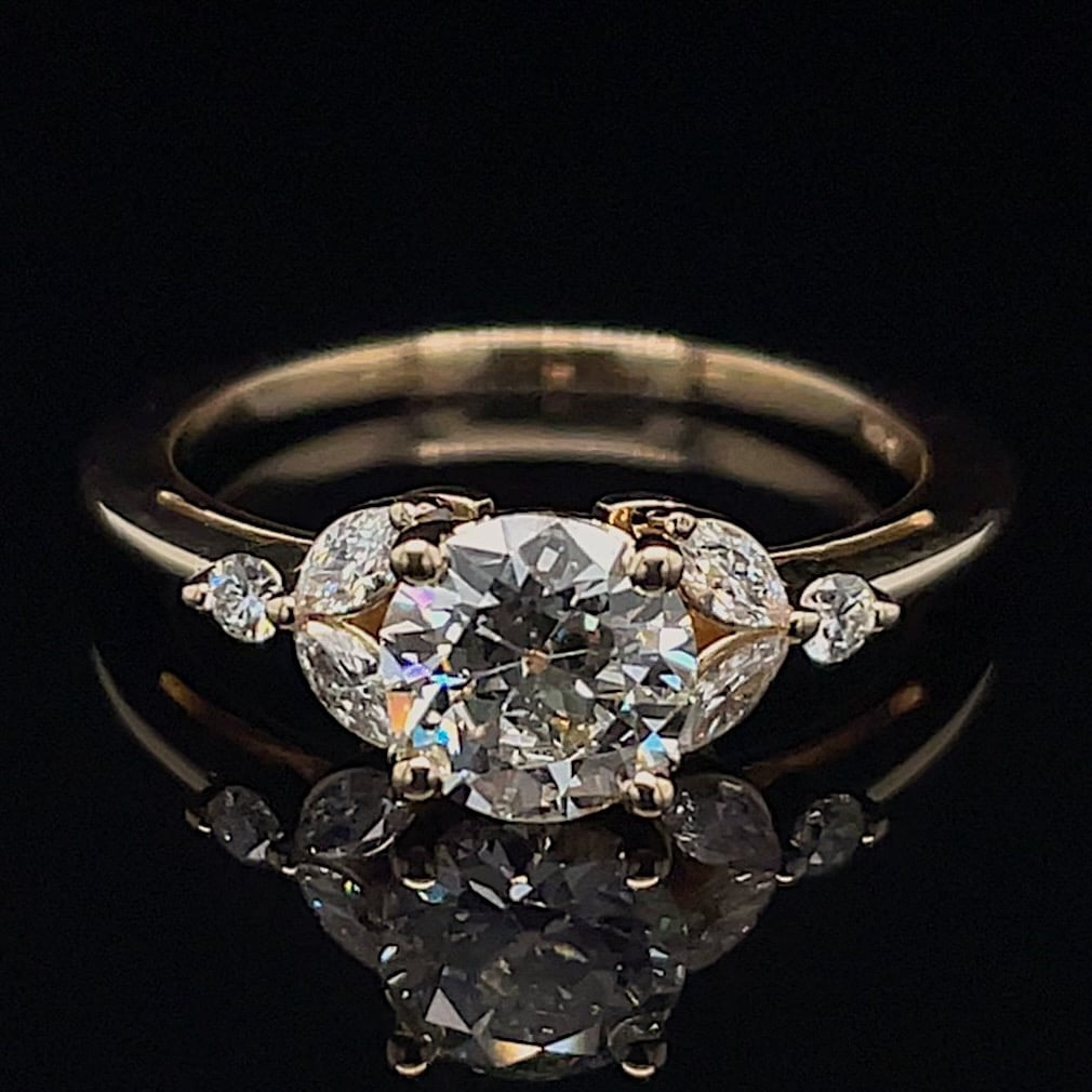 Engagement ring with a large round center diamond and small side stones in a gold setting on a black background, shown from above.