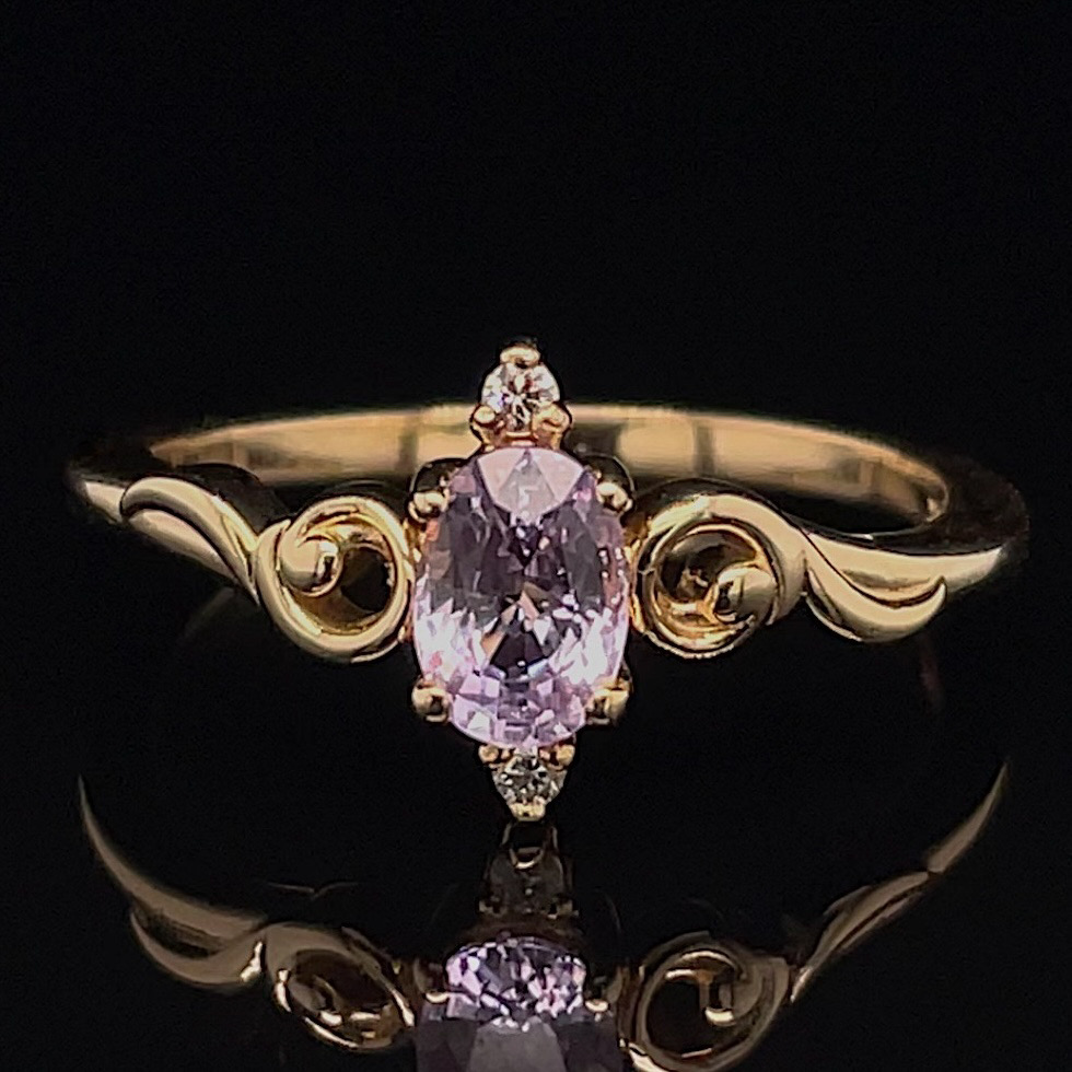 Gold ring with an oval lavender gemstone and decorative scrolling on the band against a black background.