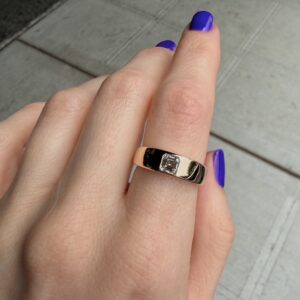 Close-up of a hand with purple nail polish wearing a gold ring with a small square diamond centerpiece.