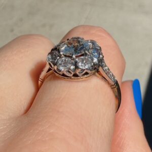 Cluster diamond ring on a finger, rose-gold band with multiple small diamonds forming a floral cluster, viewed from above.