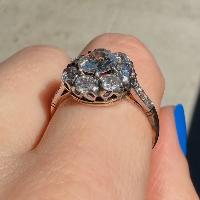 Cluster diamond ring on a finger, rose-gold band with multiple small diamonds forming a floral cluster, viewed from above.