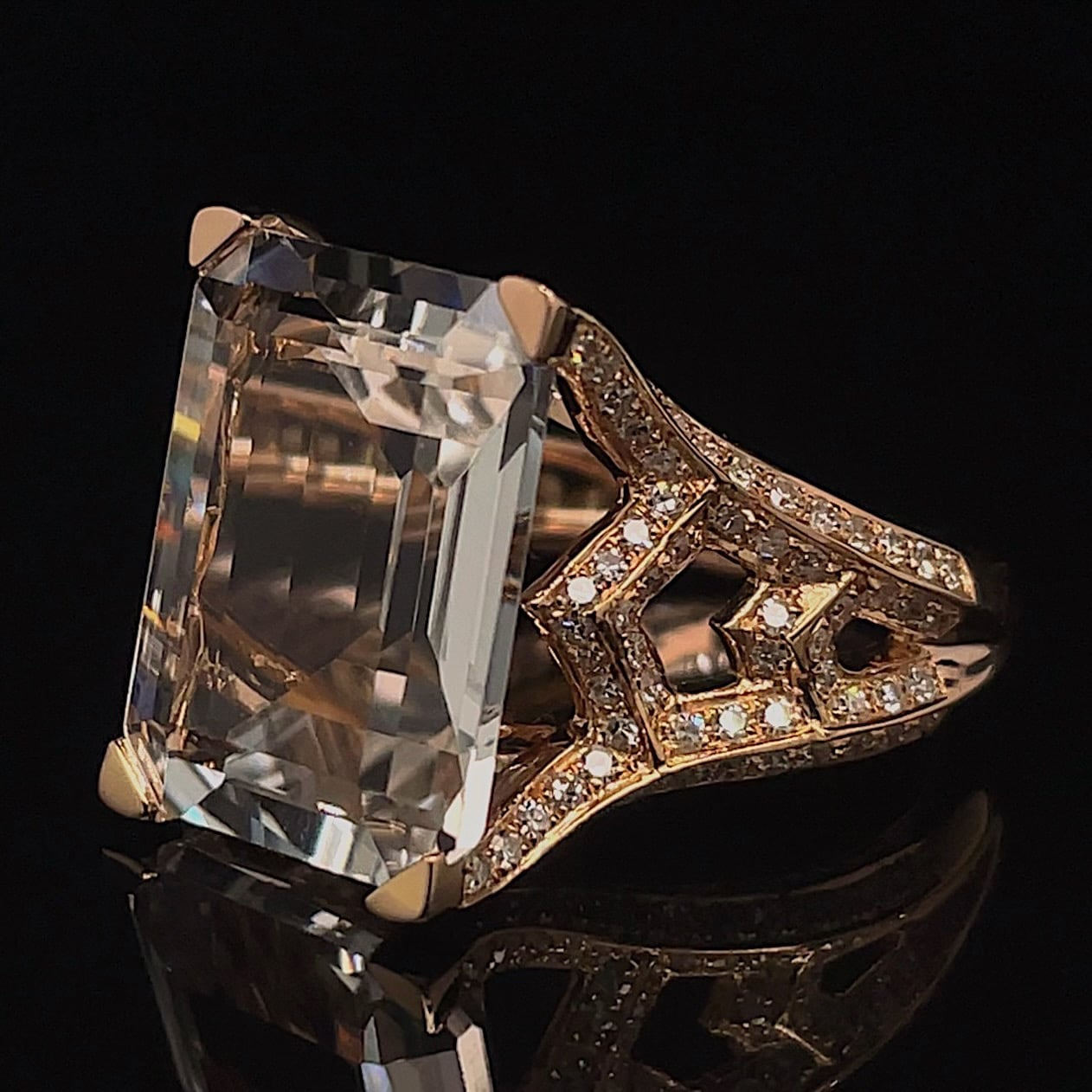 Gold ring with a massive rectangular princess-cut diamond centerpiece and pavé diamond band against a black background.