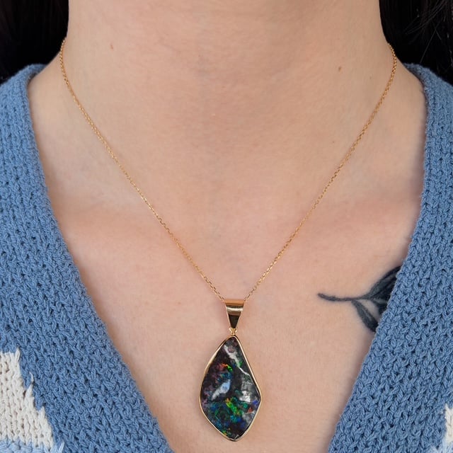 Gold chain necklace with a teardrop-shaped iridescent pendant resting on the chest.