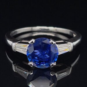 Engagement ring with a large round blue sapphire centerpiece and baguette diamond side stones on a silver band
