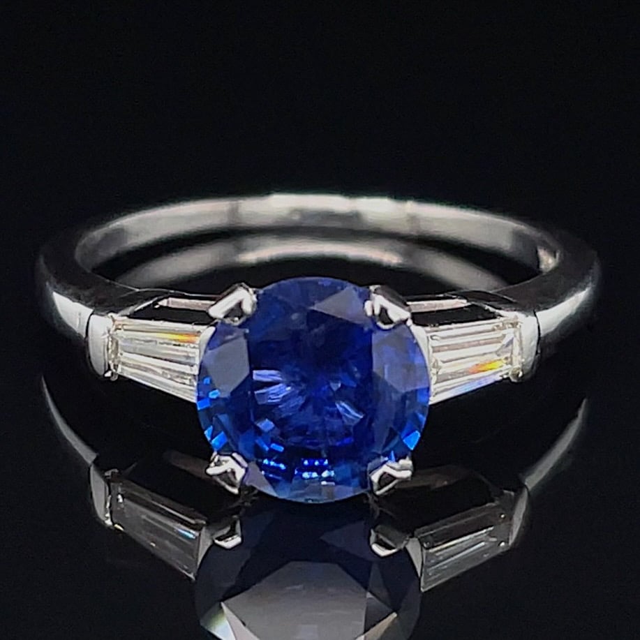 Engagement ring with a large round blue sapphire centerpiece and baguette diamond side stones on a silver band
