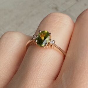 Rose gold ring with an oval green gemstone and small side stones worn on a finger.
