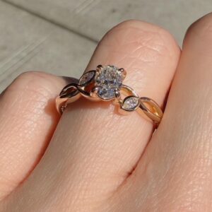 Gold ring with a round central diamond and marquise-cut side stones on a finger, in sunlight.