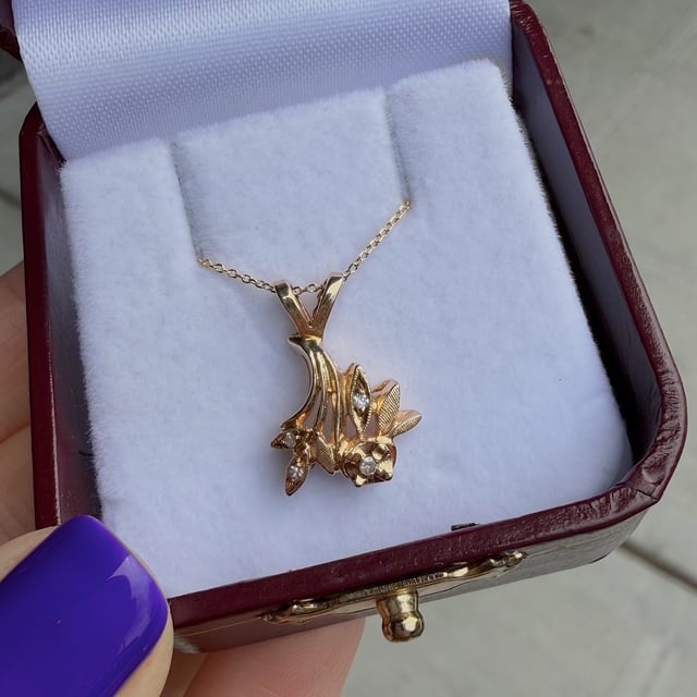 Gold pendant necklace in a red jewelry box; floral design with leaves and small stones.
