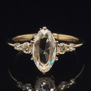 Gold ring with a large marquise-cut center diamond and smaller side stones on a black background.