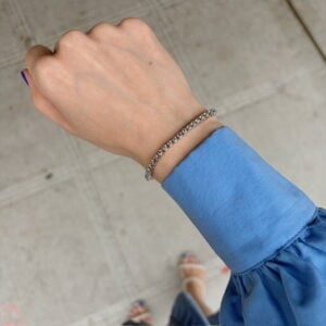Close-up of a wrist wearing a silver braided bracelet with a blue long-sleeve cuff against a concrete background.