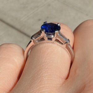 Rose-gold ring featuring a deep blue oval sapphire held by four prongs on a finger (close-up)