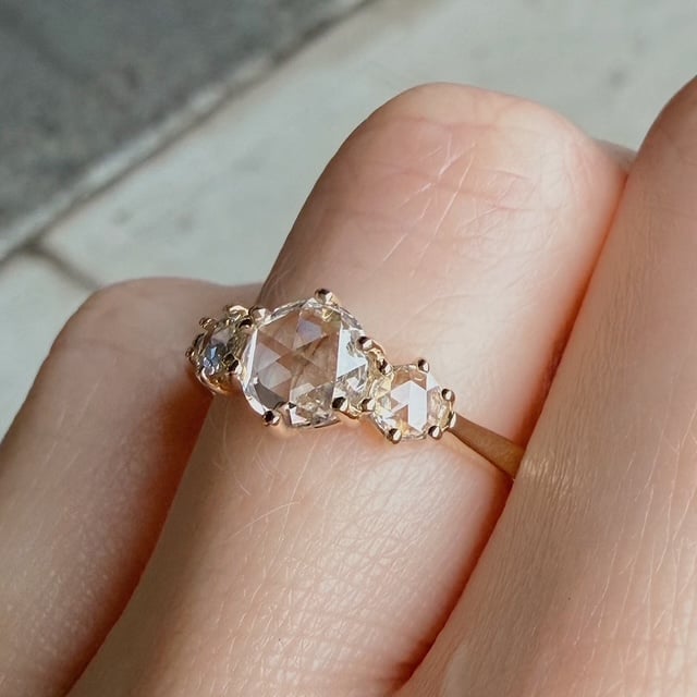 Gold ring on a finger with a large central diamond flanked by two smaller stones on a slim band.