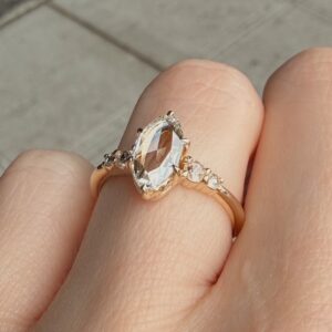 Close-up of a rose gold ring with an oval center gem and small side stones, worn on a finger.