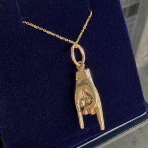 Gold pendant necklace on a chain featuring a vertical, cage-like frame with a stylized animal figure inside, resting on dark fabric.