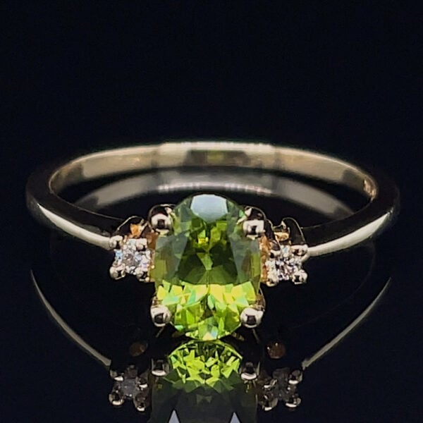 Emerald-green central gemstone ring with two diamond side stones on a metallic band, set against a black reflective background.