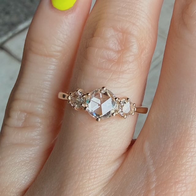 Delicate gold ring with a large central crystal flanked by two smaller stones on a finger.