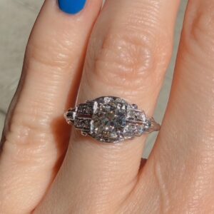 Close-up of a halo diamond engagement ring on a finger with bright blue nail polish.