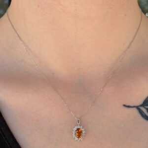 Silver chain necklace with an orange oval pendant surrounded by small clear stones resting on the neck.
