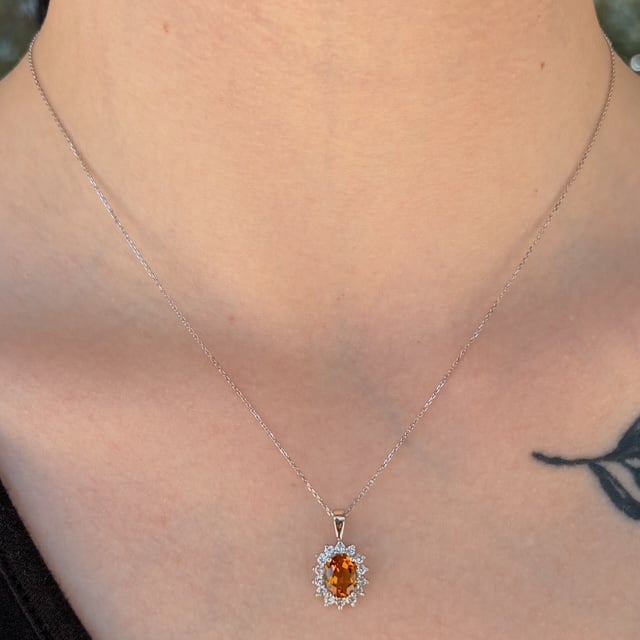 Silver chain necklace with an orange oval pendant surrounded by small clear stones resting on the neck.