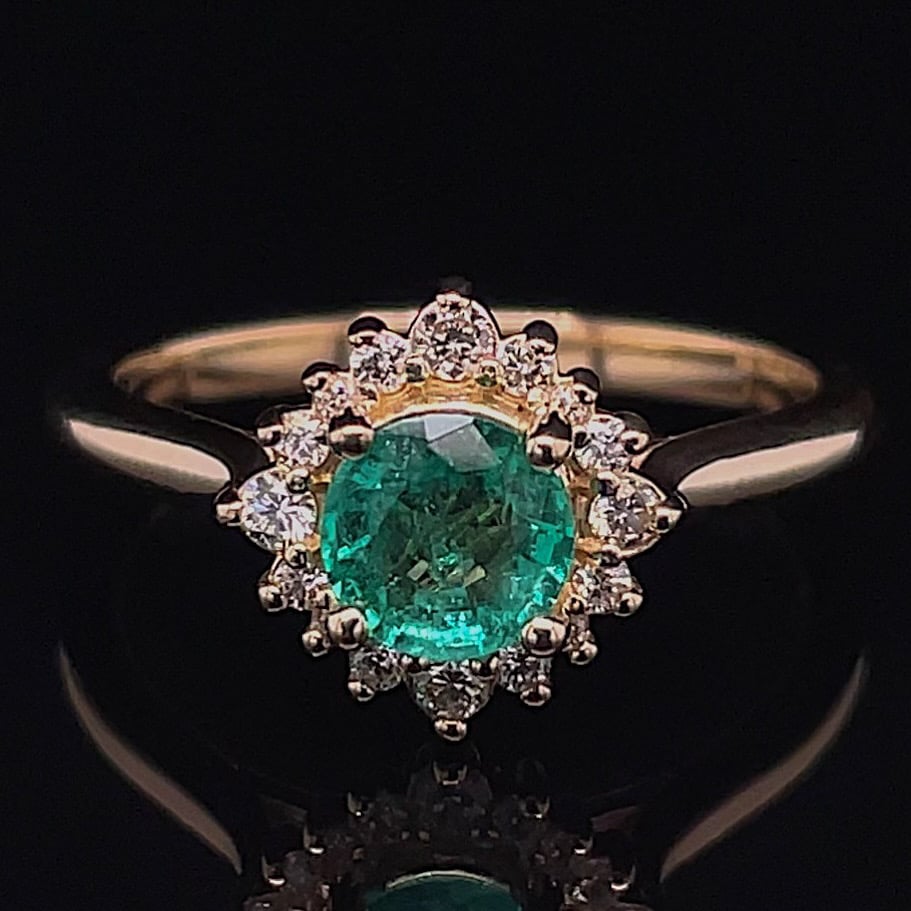 Gold ring with an emerald center surrounded by a diamond halo on a black background