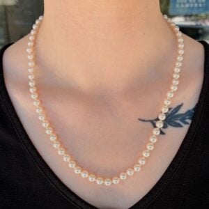 Pearl necklace resting on the neck over a black top, with a small black leaf tattoo on the upper chest area