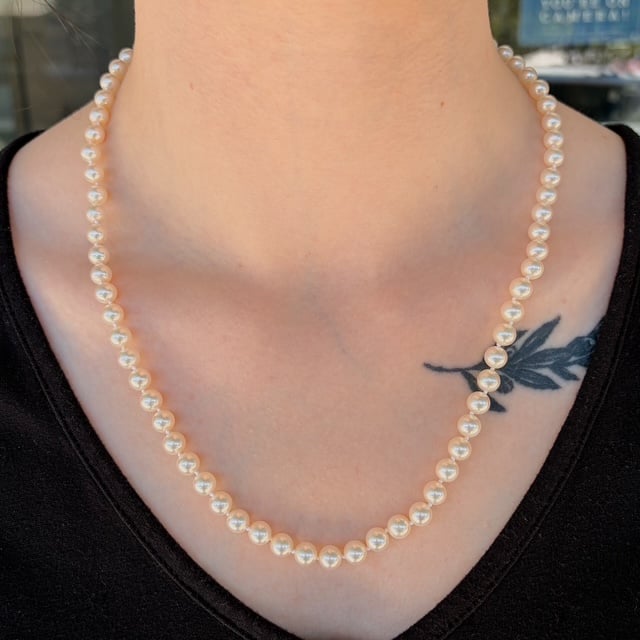 Pearl necklace resting on the neck over a black top, with a small black leaf tattoo on the upper chest area