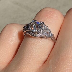 Close-up of a silver ring with a large central diamond and smaller surrounding stones on a finger.