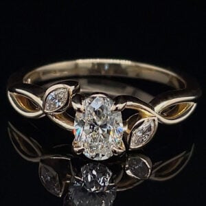 Gold ring with a large oval-cut center diamond and marquise side stones on a dark background.