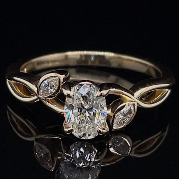 Gold ring with a large oval-cut center diamond and marquise side stones on a dark background.