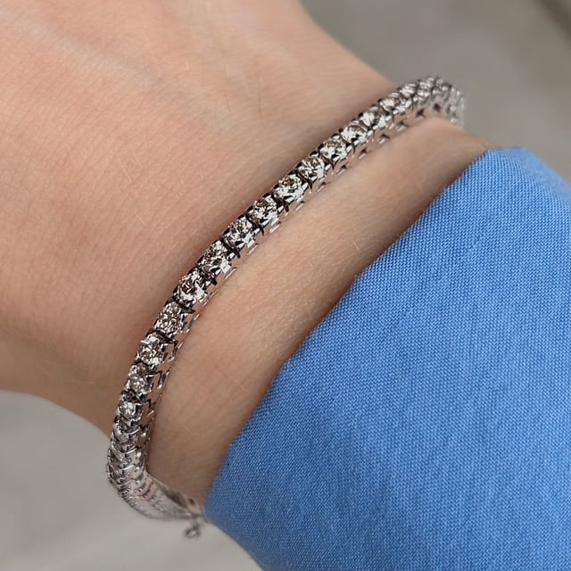 Silver diamond tennis bracelet on a wrist, with a blue fabric cuff nearby.