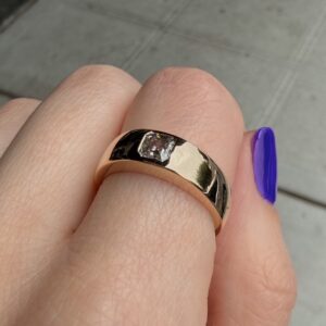 Close-up of a gold ring with a small square-cut diamond on a finger with purple nail polish.