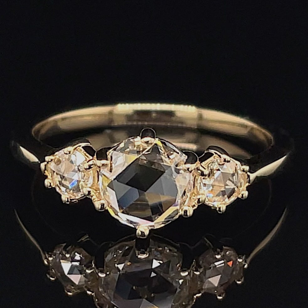 Three-stone ring with a large central dark gemstone and two clear side stones on a gold band.