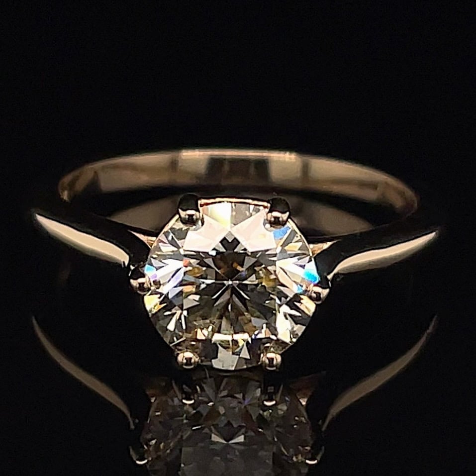 Diamond engagement ring with a round brilliant-cut diamond in a four-prong setting on a slender metal band, against a black background.