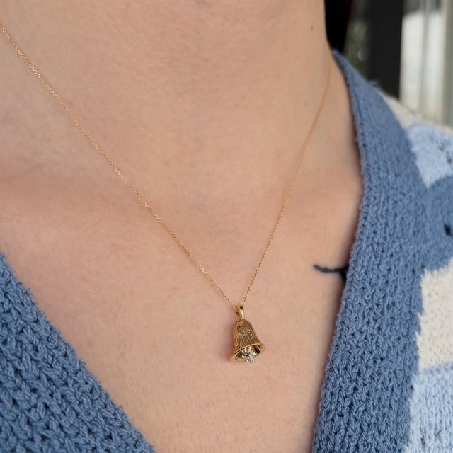 Close-up of a gold chain necklace with a tiny pendant that resembles a tassel or bell, resting on a blue knit top.