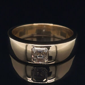 Gold band ring with a bezel-set square-cut diamond, shown on a glossy black surface with its facets reflecting light.