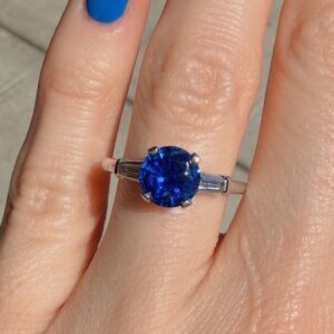 Ring with a round blue gemstone on a finger, blue nail polish visible
