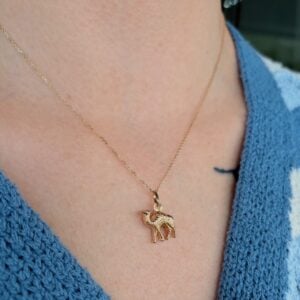 Gold chain necklace with a small elephant pendant resting on a blue knit top (photo close-up).