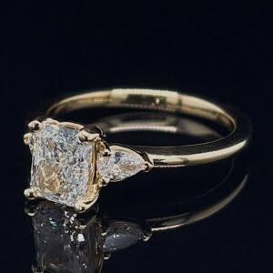 Women’s diamond ring with a cushion-cut center stone and two side stones on a gold band, on a black reflective surface