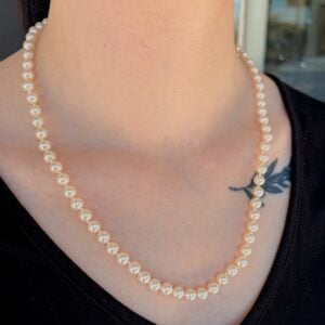 Close-up of a pearl bead necklace worn on a black top, with a small leaf tattoo on the collarbone area visible beside the necklace.
