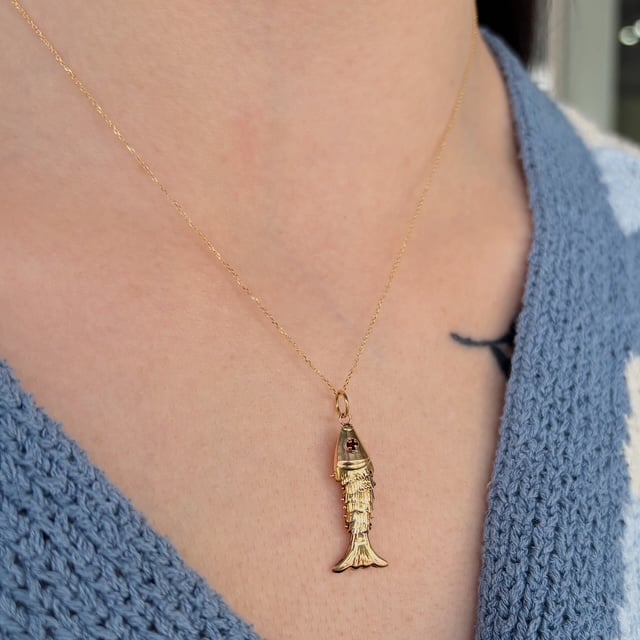 Gold fish pendant necklace on a blue knit sweater, close-up of the chest area.